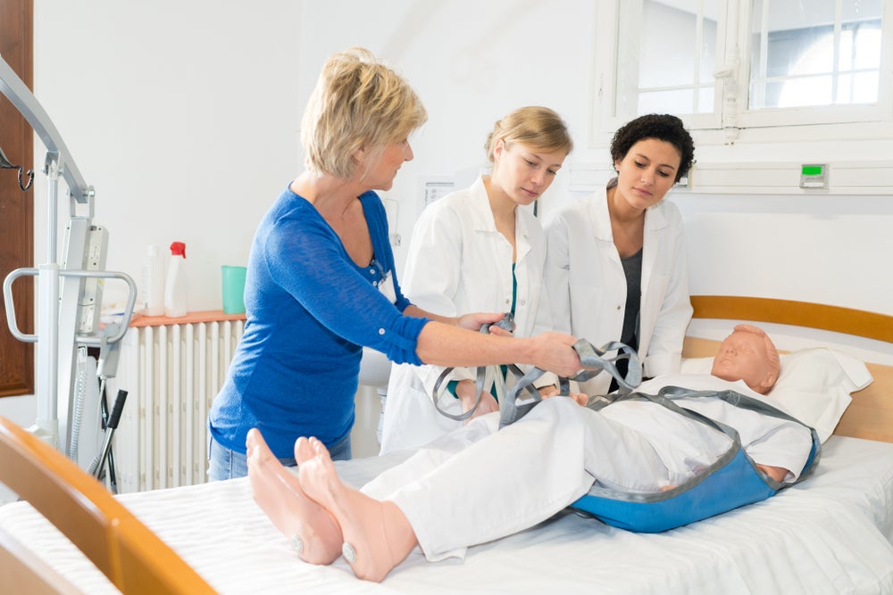 Student nurses gather around a hospital bed with a nurse educator.